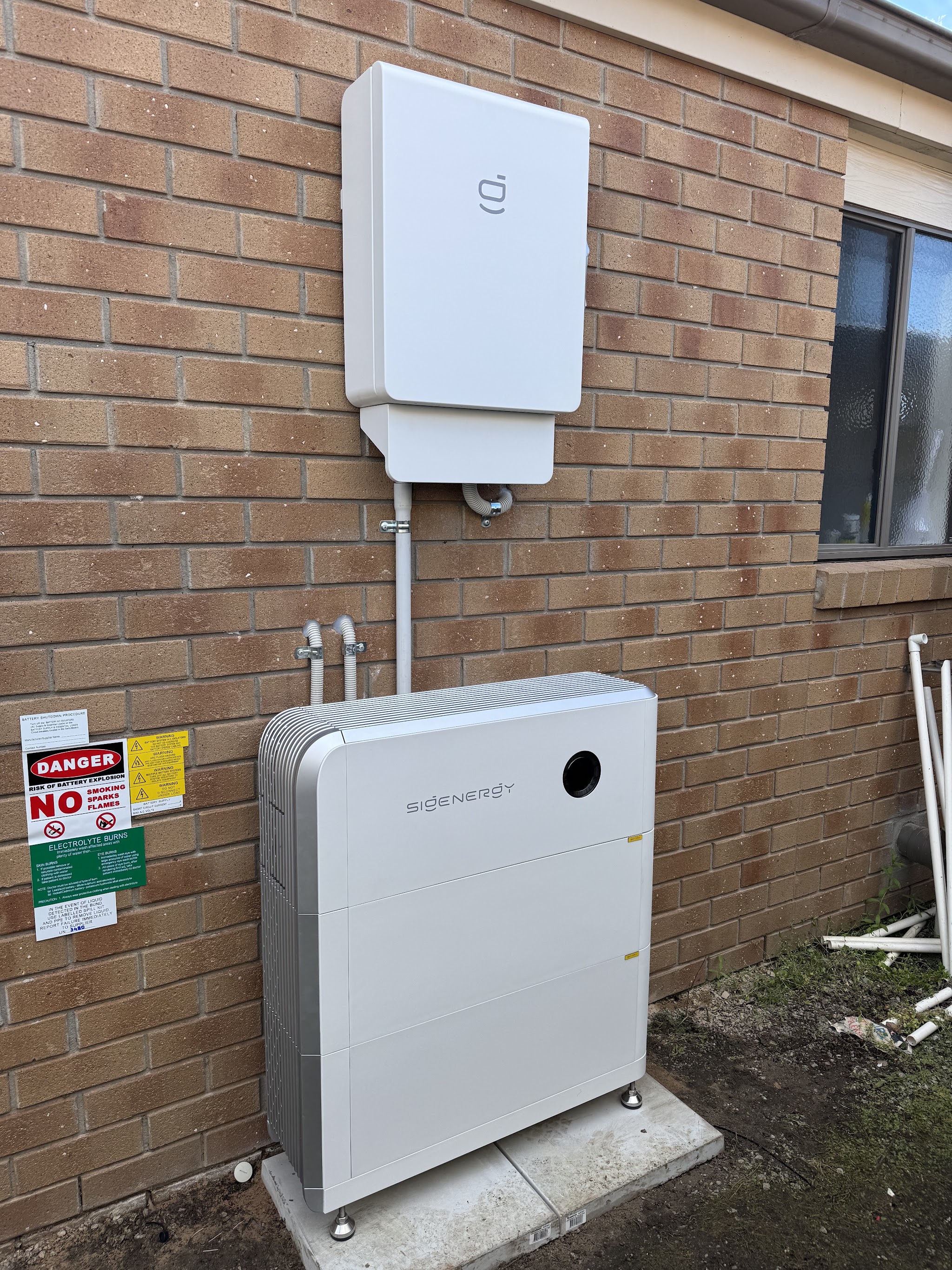 Home battery and inverter installed on a brick wall with compliance signage